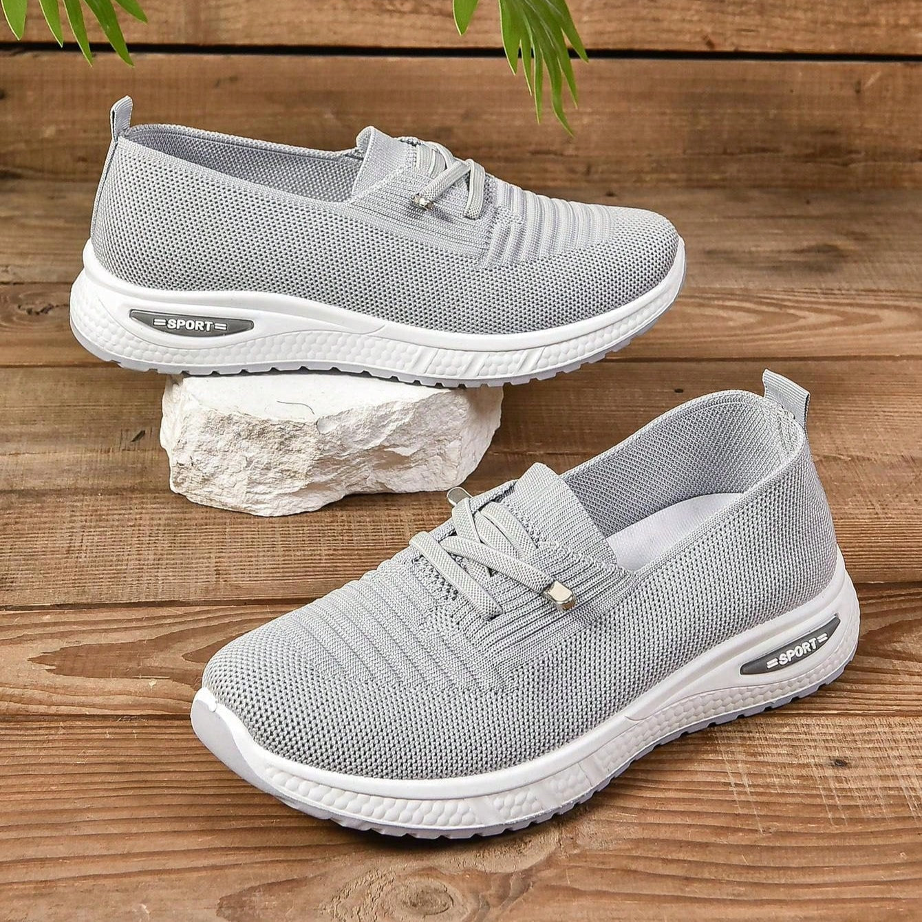Scarpe da ginnastica grigie su sfondo di legno, design traspirante in tessuto a rete, suola bianca antiscivolo, ideali per sport e tempo libero.