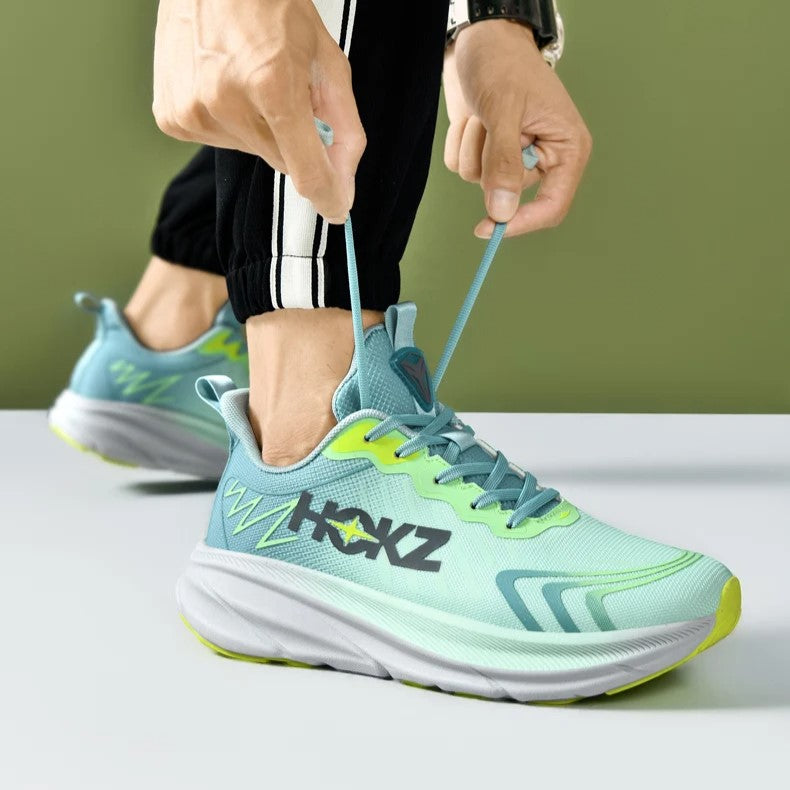 Scarpe da corsa verdi e blu con logo, suola ammortizzata e lacci, indossate da una persona su sfondo verde. Scarpe sportive moderne e comode.