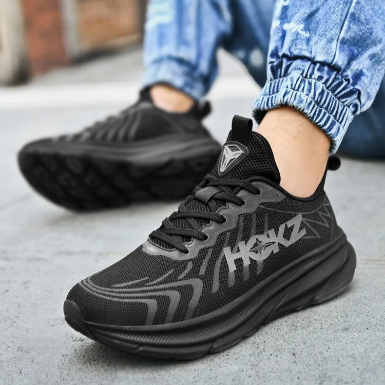 Scarpe da ginnastica nere moderne su pavimento grigio, indossate con jeans chiari. Design sportivo, suola spessa, perfette per attività all'aperto.