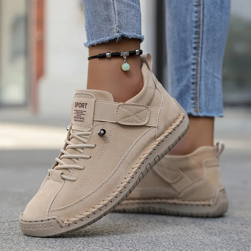 Scarpe sportive beige da donna in pelle scamosciata, abbinate a jeans aderenti. Design casual, suola antiscivolo, perfette per passeggiate urbane.