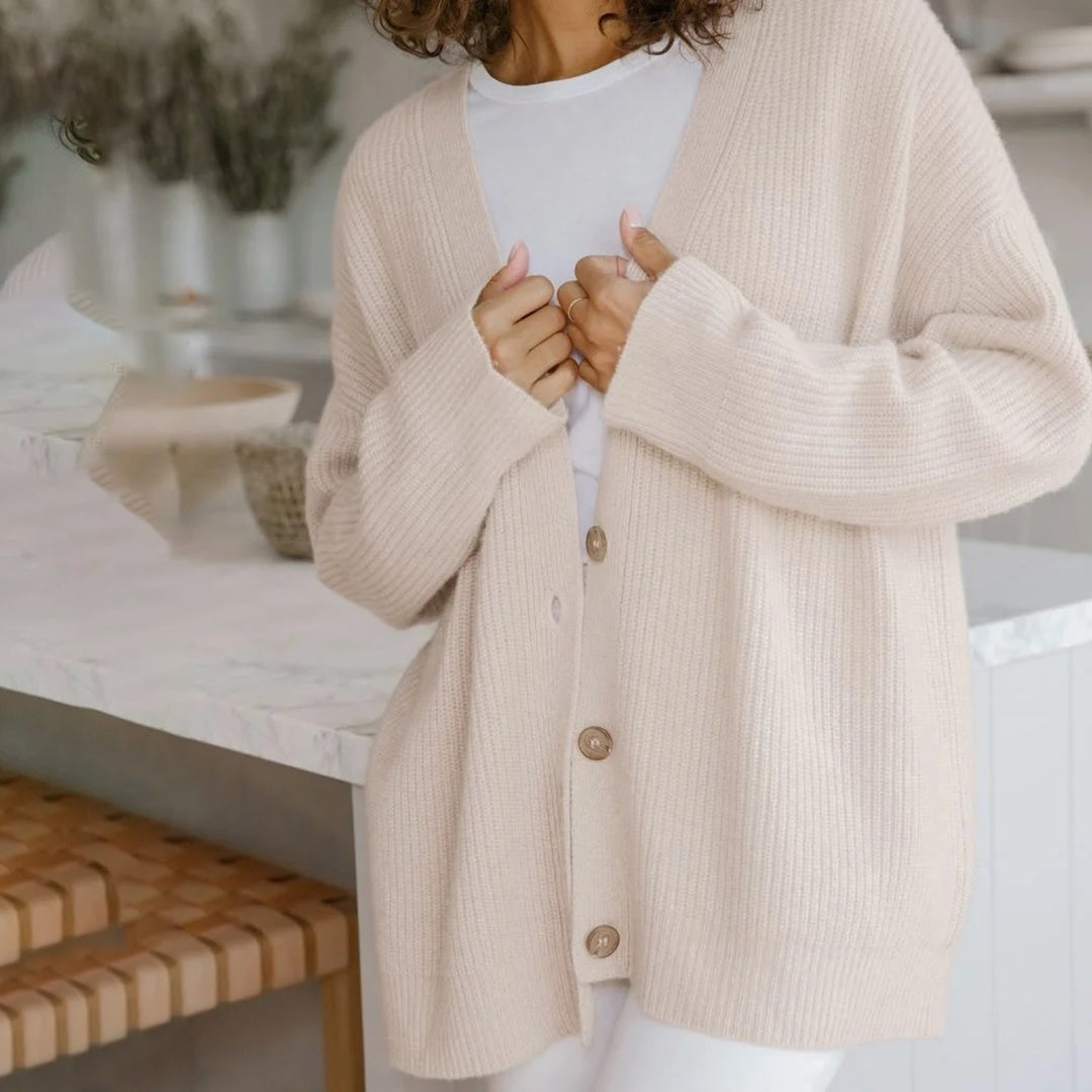 Donna con cardigan beige in maglia, t-shirt bianca, in cucina moderna. Moda autunnale, abbigliamento casual, stile confortevole.