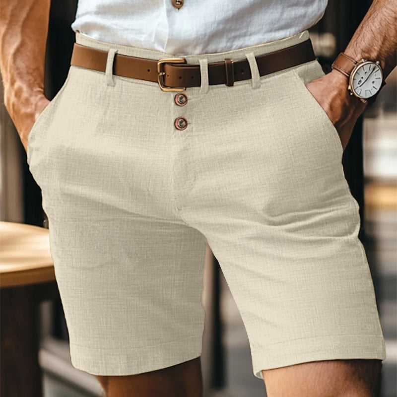 Uomo in pantaloncini beige eleganti, camicia bianca, cintura marrone, orologio da polso, mani in tasca. Moda estiva maschile casual.
