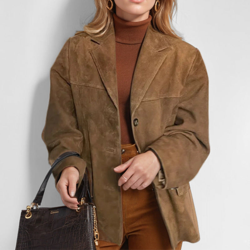 Giacca in pelle scamosciata marrone da donna, abbinata a dolcevita marrone e pantaloni coordinati. Borsa a mano nera con dettagli dorati.