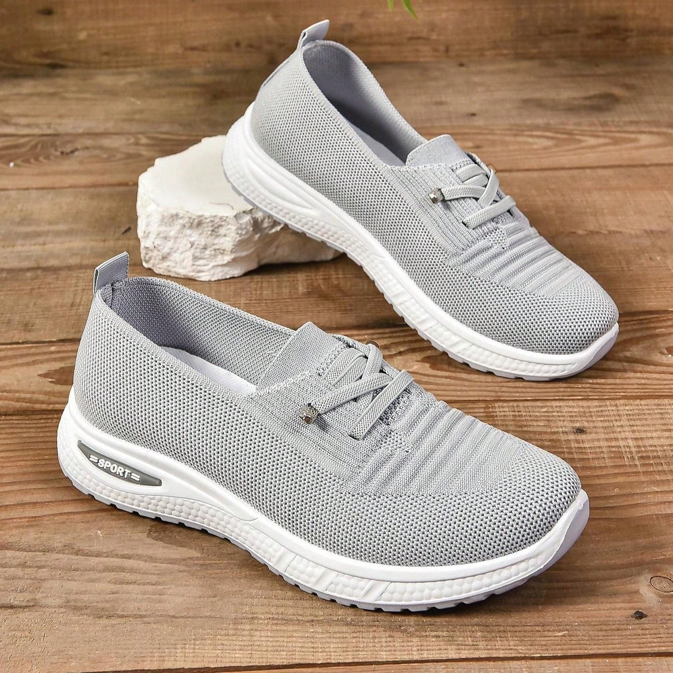 Scarpe da ginnastica grigie su sfondo di legno, design traspirante, suola bianca, ideali per sport e tempo libero, moda casual, comfort quotidiano.