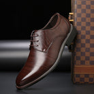 Scarpa elegante da uomo in pelle marrone lucida, con lacci e suola nera, posizionata accanto a una valigia a scacchi. Scarpe formali di lusso.