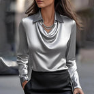 Donna con camicia di seta grigia e collana elegante, sfondo urbano sfocato. Moda femminile, abbigliamento elegante, stile sofisticato.