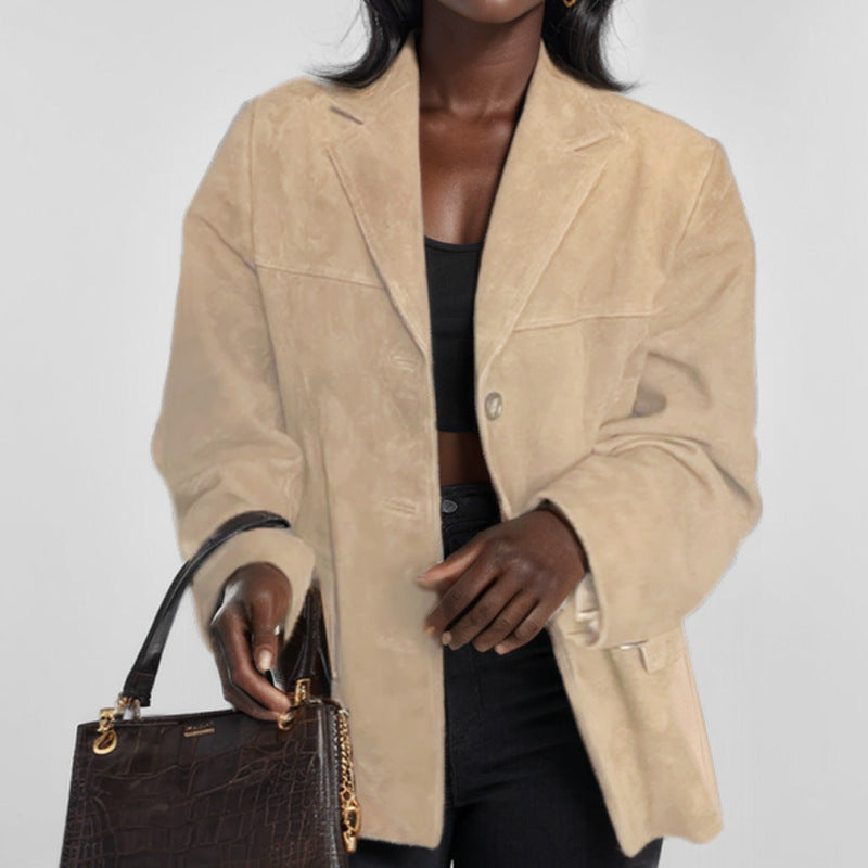 Donna con giacca beige in pelle scamosciata, top nero e borsa marrone con dettagli dorati. Moda autunnale elegante e sofisticata.