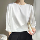 Donna in camicetta bianca elegante, maniche a tre quarti, tiene una piccola borsa bianca. Moda minimalista, abbigliamento casual chic.