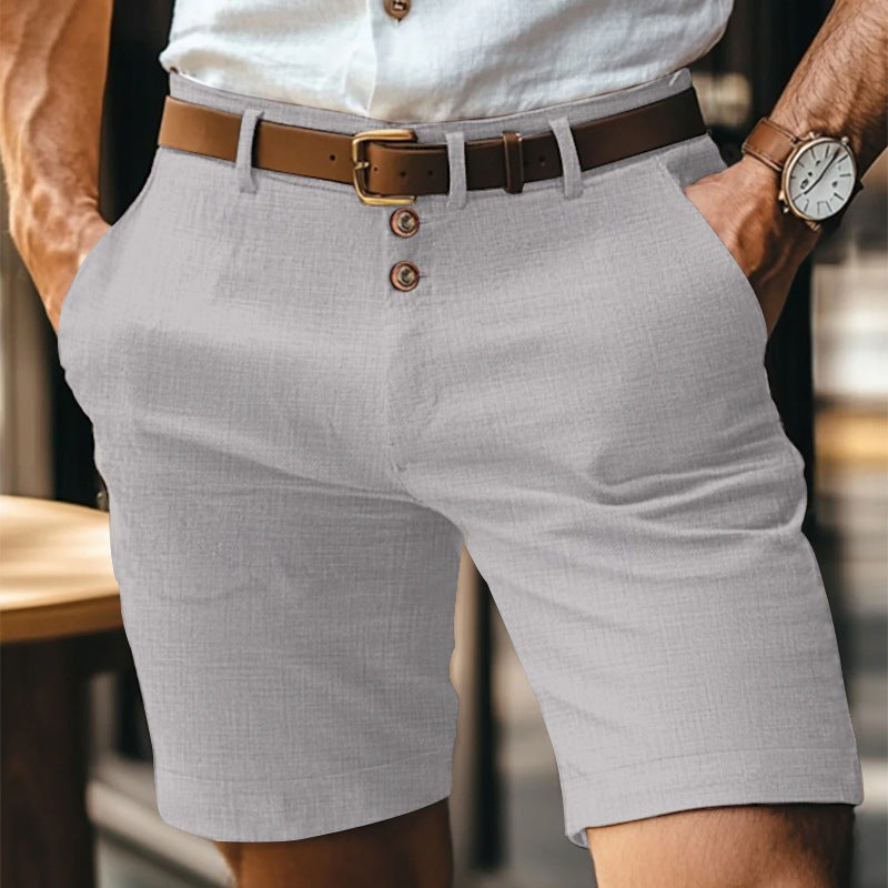 Uomo in pantaloncini grigi eleganti, camicia bianca, cintura marrone, orologio al polso. Moda estiva maschile, abbigliamento casual chic.