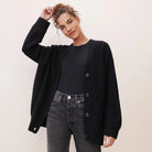 Donna con cardigan nero oversize, maglietta nera e jeans grigi. Moda casual autunnale, abbigliamento femminile elegante e confortevole.