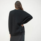 Donna di spalle indossa maglione nero oversize in lana, abbinato a gonna lunga. Moda autunno inverno, abbigliamento casual elegante.