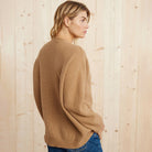 Donna con maglione beige in lana, profilo laterale, sfondo in legno chiaro. Moda autunnale, abbigliamento casual, stile confortevole.