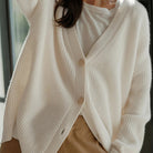 Cardigan bianco in lana morbida con bottoni, indossato su maglietta bianca e pantaloni beige. Moda autunnale, abbigliamento casual elegante.