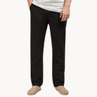 Person wearing black linen pants and beige slippers on a white background