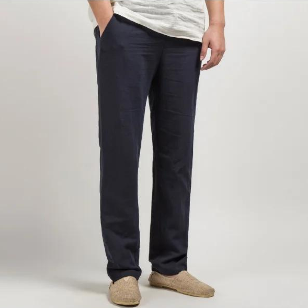 Person wearing navy linen pants and beige shoes on a plain background