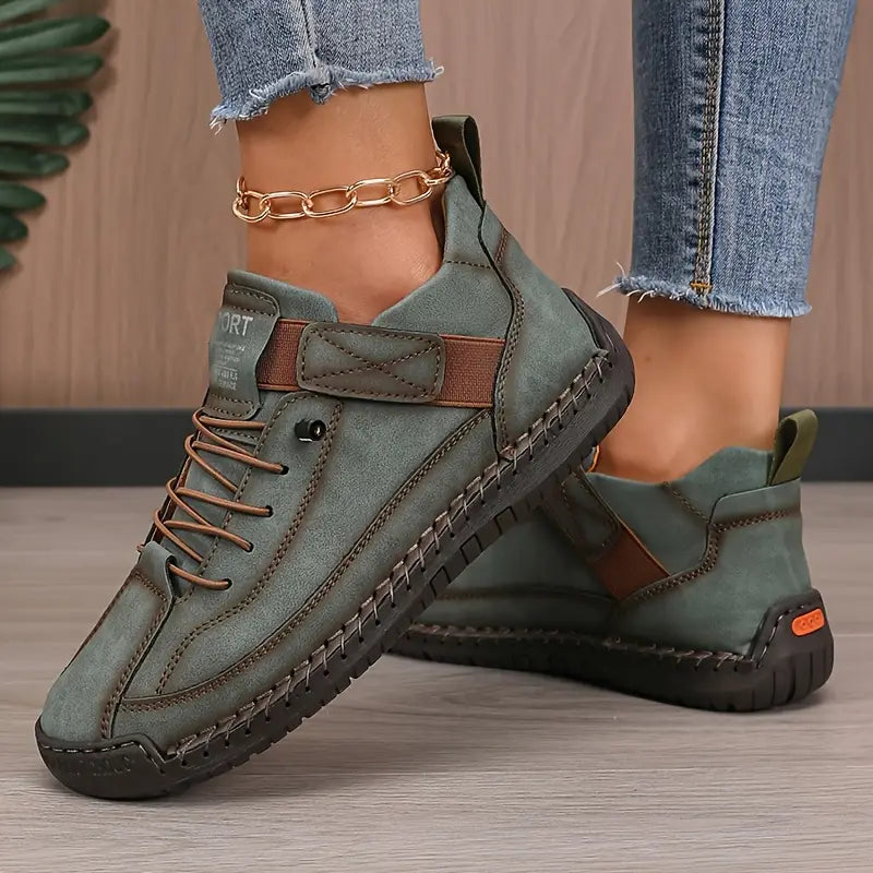 Scarpe sportive da donna in pelle verde con suola antiscivolo nera, dettagli marroni e lacci, indossate con jeans. Calzature casual eleganti.