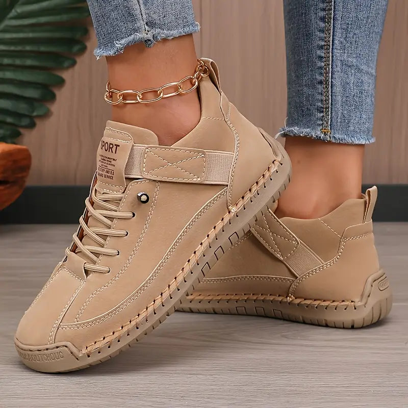 Scarpe sportive beige da donna, design casual con suola in gomma antiscivolo, lacci e cinturino, abbinate a jeans aderenti e cavigliera dorata.