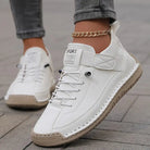 Scarpe da ginnastica bianche da donna con suola beige, indossate su pavimento in pietra. Design moderno, casual, con cavigliera dorata.