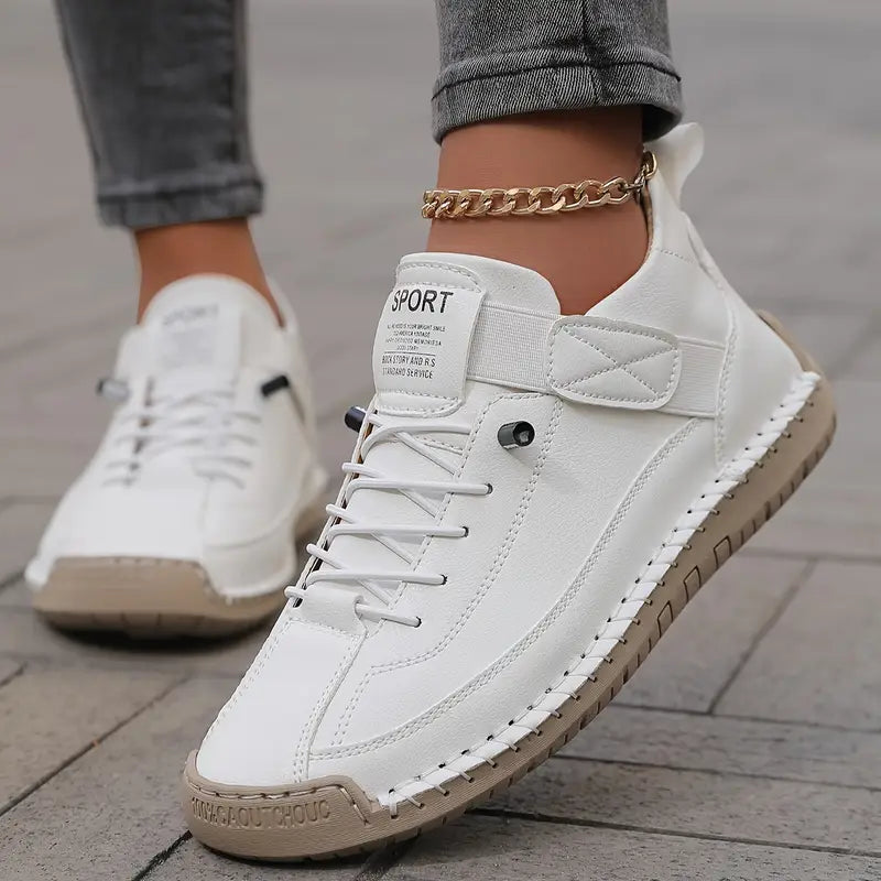 Scarpe da ginnastica bianche da donna con suola beige, indossate su pavimento in pietra. Design moderno, casual, con cavigliera dorata.