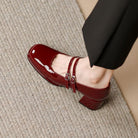 Scarpa Mary Jane in vernice rossa con tacco medio, doppio cinturino, indossata su tappeto beige. Elegante calzatura donna, moda autunno.