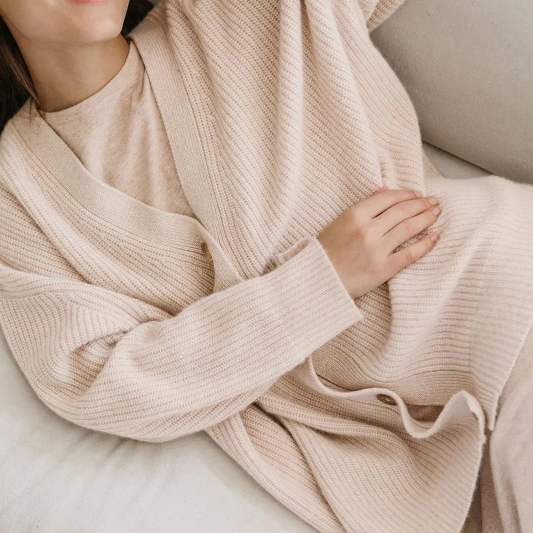 Donna indossa cardigan beige in maglia su divano, moda autunnale, abbigliamento casual elegante, tessuto morbido e confortevole, stile minimalista.