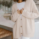 Donna con cardigan beige in maglia, t-shirt bianca, in cucina moderna. Moda autunnale, abbigliamento casual, stile confortevole.