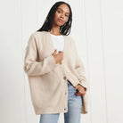 Donna con cardigan beige oversize, maglietta bianca e jeans chiari. Moda casual autunnale, stile confortevole ed elegante. Sfondo bianco minimalista.