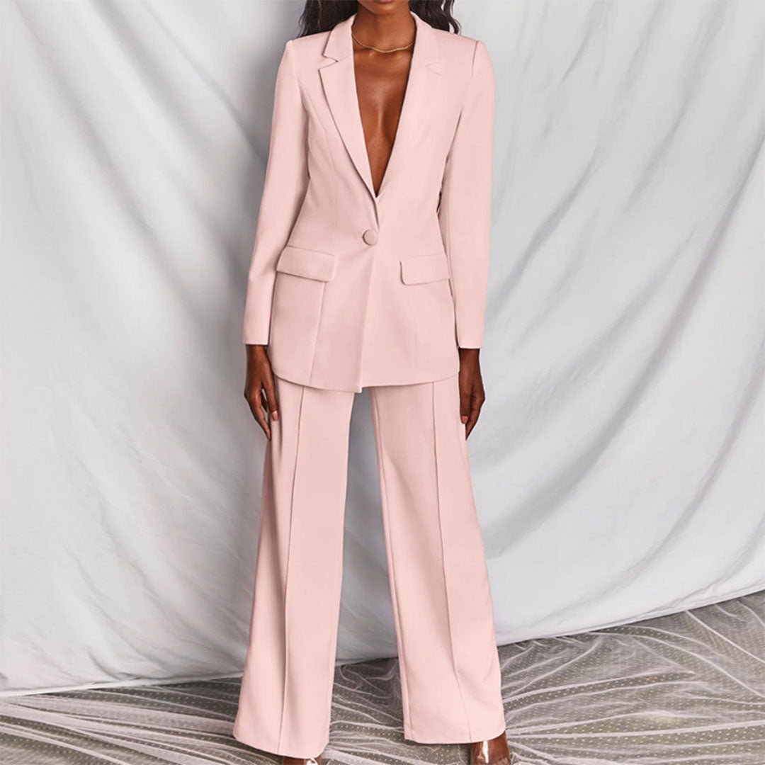 Donna in elegante completo pantalone rosa chiaro, giacca con un bottone, sfondo drappeggiato. Moda femminile, abbigliamento formale, tendenze 2023.