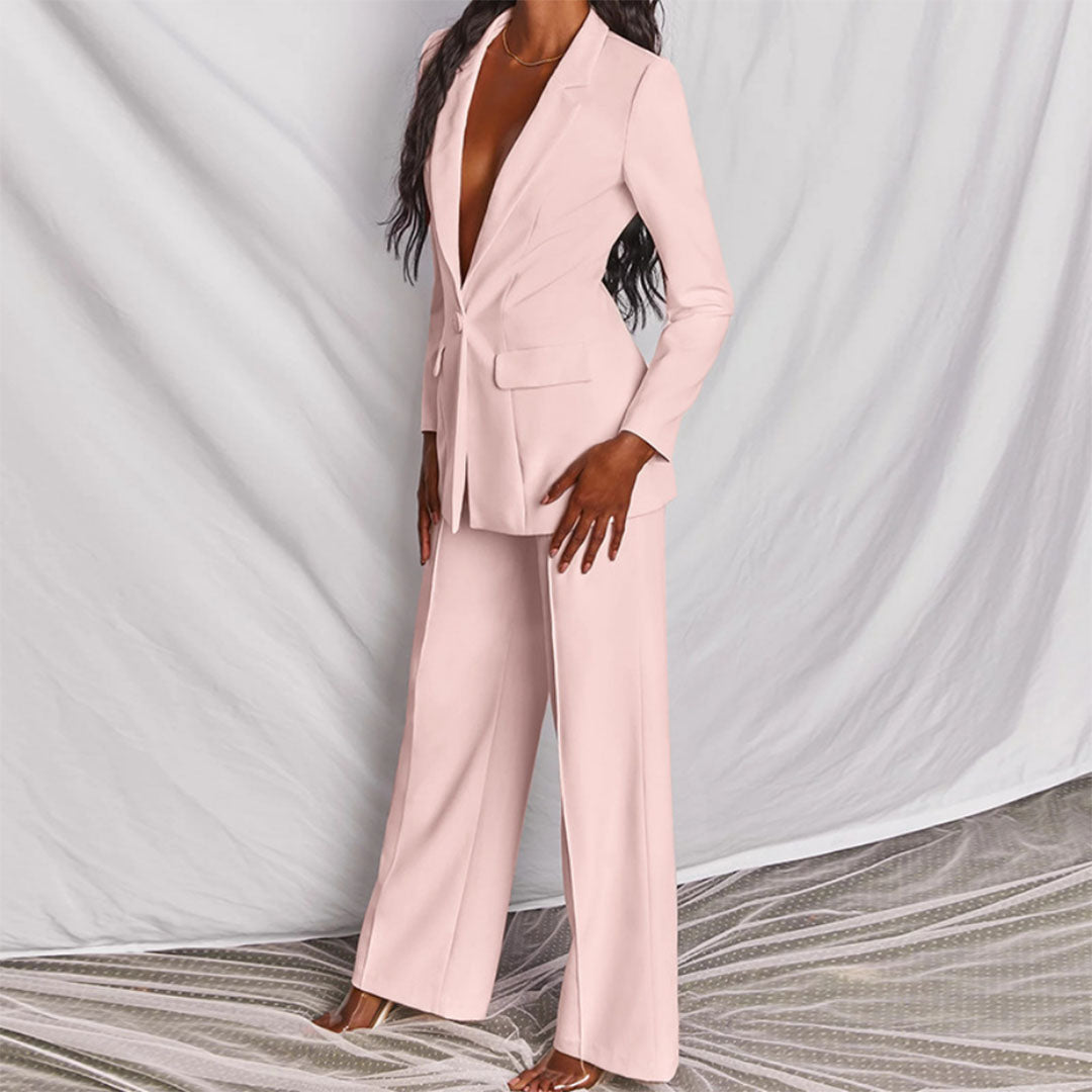 Donna in elegante tailleur pantalone rosa, giacca lunga e pantaloni larghi, su sfondo bianco. Moda femminile, abbigliamento formale, stile sofisticato.