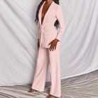 Donna in elegante tailleur pantalone rosa, giacca lunga e pantaloni larghi, su sfondo bianco. Moda femminile, abbigliamento formale, stile sofisticato.