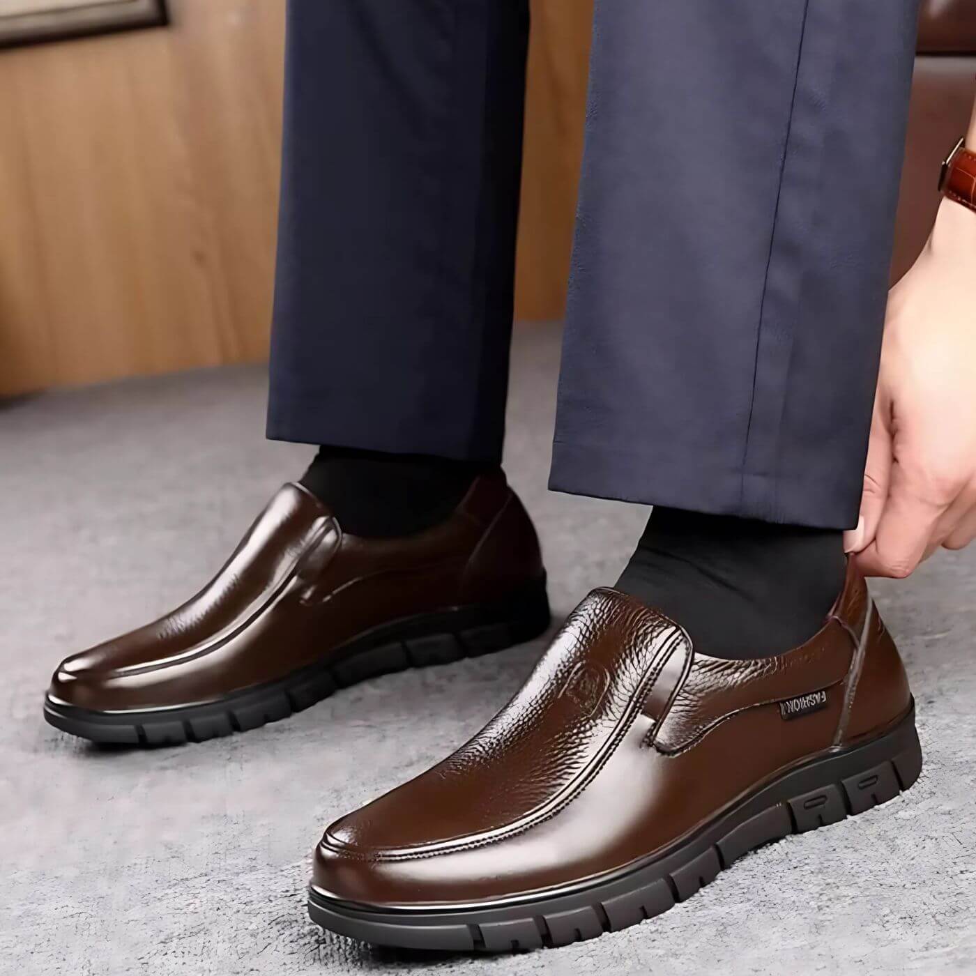 Scarpe eleganti da uomo in pelle marrone, indossate con pantaloni blu scuro. Design slip-on, suola robusta, ideali per look formale e casual.