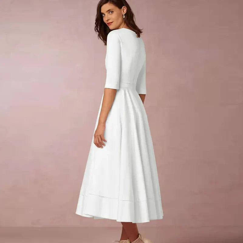 Donna in abito bianco elegante, maniche a tre quarti, lunghezza midi, sfondo rosa. Moda femminile, abbigliamento formale, stile classico.