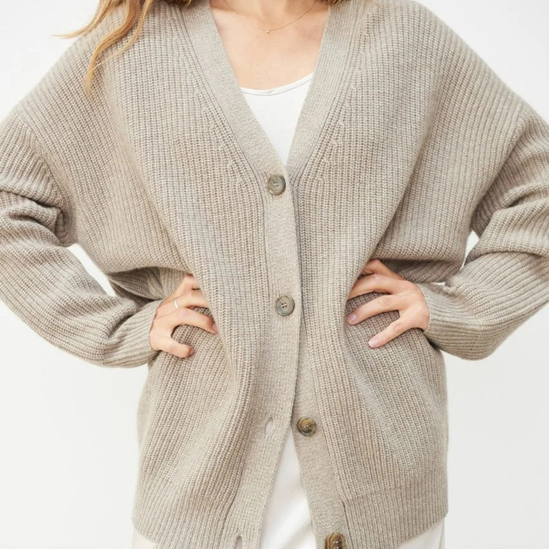 Donna indossa un cardigan beige oversize in maglia con bottoni, su abito bianco. Moda autunnale, abbigliamento casual elegante, stile confortevole.