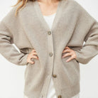 Donna indossa un cardigan beige oversize in maglia con bottoni, su abito bianco. Moda autunnale, abbigliamento casual elegante, stile confortevole.