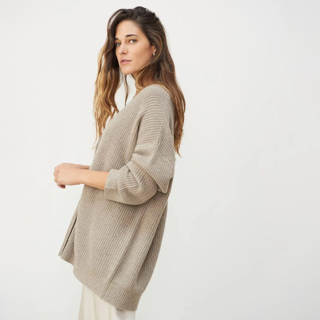 Donna con maglione oversize beige, posa laterale su sfondo bianco. Moda autunnale, abbigliamento casual, stile minimalista.