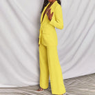 Completo donna elegante giallo, giacca e pantaloni larghi, moda contemporanea, abbigliamento formale, tessuto liscio, sfondo bianco.