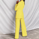 Donna in elegante completo giallo, giacca e pantaloni, su sfondo bianco. Moda femminile, abbigliamento formale, tendenze colore 2023.