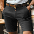Uomo in pantaloncini eleganti neri con cintura marrone e camicia bianca, orologio al polso, moda estiva maschile, abbigliamento casual chic.