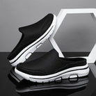 Scarpe slip-on nere da uomo con suola bianca, design sportivo e traspirante, posizionate su sfondo grigio con elemento geometrico bianco.