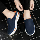 Scarpe slip-on blu scuro con suola bianca e dettagli arancioni, indossate su piastrelle nere. Calzature casual estive, comode e traspiranti.