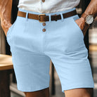 Uomo in pantaloncini azzurri eleganti, camicia bianca, cintura marrone, orologio al polso. Moda estiva maschile, abbigliamento casual chic.