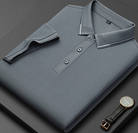 Camicia polo grigia piegata su sfondo nero, con colletto a contrasto e bottoni, accanto a un orologio elegante. Moda uomo, abbigliamento casual.
