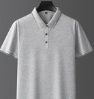 Maglietta polo grigia in cotone, maniche corte, colletto classico, bottoni frontali, design semplice ed elegante, ideale per abbigliamento casual.