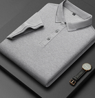 Camicia polo grigia piegata su sfondo nero, con orologio elegante accanto. Moda uomo, abbigliamento casual, stile minimalista.