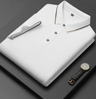 Camicia polo bianca piegata su sfondo nero, con dettagli a righe sul colletto e polsini. Orologio elegante con cinturino in pelle accanto.