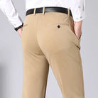Pantaloni eleganti beige da uomo, tasche posteriori con bottoni, camicia bianca, cintura nera. Moda maschile, abbigliamento formale.